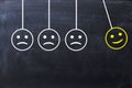 Spread happiness concept with happy and sad faces on newtonÃ¢â¬â¢s cradle on blackboard